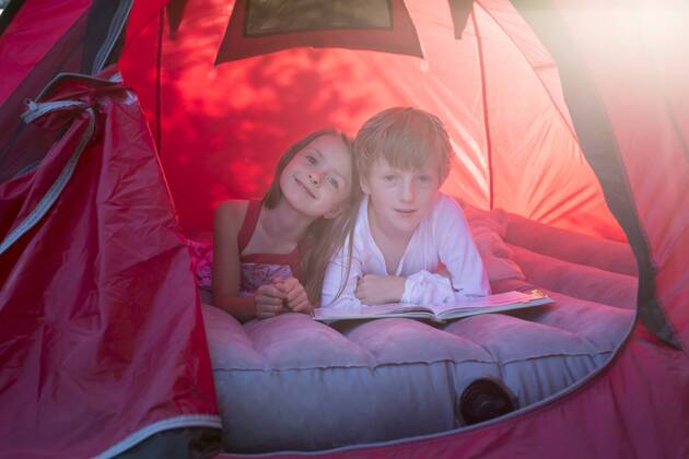 Portrait of brother and sister lying in a red tent with a book model released Symbolfoto  SARF001931