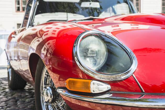 Detail eines Jaguar E-Type Baujahr 1964 in rot, Frontpartie mit Scheinwerfer, Blinker, Speichenrad und Motorhaube, Spiegelungen auf dem glänzenden Lack von Kotflügel und Kühlerhaube Sinnliche Formen
