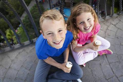 Portrait of brother and sister with ice cream cones sitting on balcony looking up to camera model released Symbolfoto  VABF000472