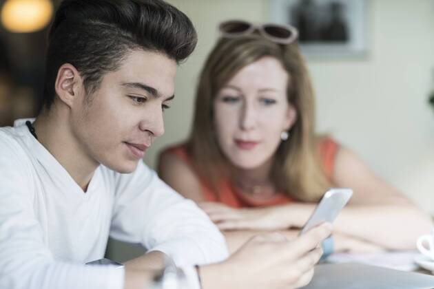 IMAGO Creative: Gesellschaft, Integration Teenage boy using cell phone with woman in background model released Symbolfoto  TAMF00888