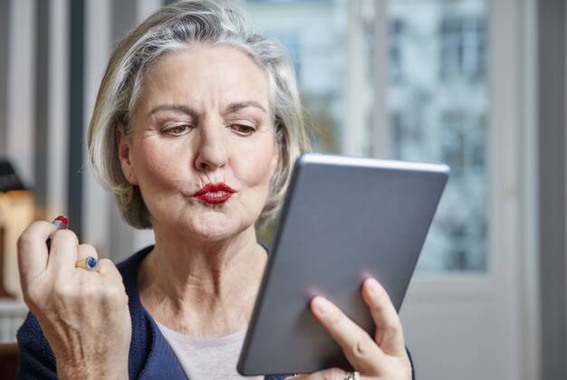 Senior woman applying lipstick holding tablet model released Symbolfoto property released  RHF01794