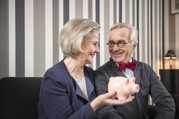 Happy senior couple sitting on couch with piggy bank model released Symbolfoto property released  RHF01775