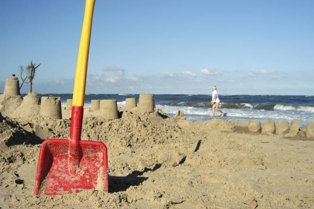 Eine rote Schaufel steckt am Strand im Sand nach dem Bau einer großen Sandburg Strandvergnügen