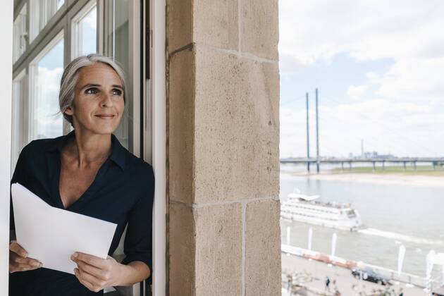 Smiling businesswoman looking out of window in waterfront office model released Symbolfoto property released  KNSF01771