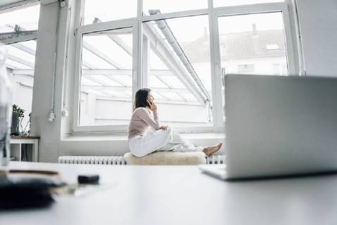 Young woman on the phone sitting on sheepskin on heater in a loft looking out of window model released Symbolfoto property released  MOEF00446