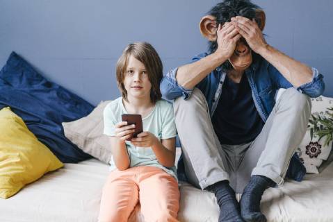 Father wearing monkey mask sitting next to son using smartphone at home model released Symbolfoto property released  KNSF03649