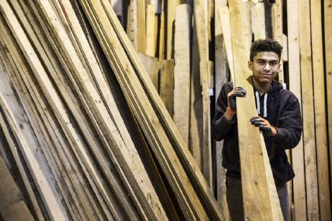 IMAGO Creative: Nächste Generation, Sozial- und klimabewusst Young man wearing work gloves standing next to a stack of wooden planks in a warehouse, carrying long pieces of wood, looking at camera. Young man wearing work gloves standing next to a stack of wooden planks in a warehouse, carrying long pieces of wood, looking at camera. 40694