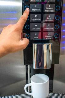 Man hand operates coffeemaker in office. Espresso cup button stands ready for coffee. Coffee machine in office kitchen