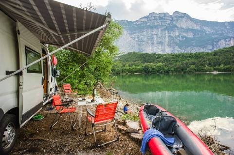 Rest in a motorhome and kayak on the shores of Lake Garda Lago di Cavedine in the province of Trento Trentino Italy A motorhome with a kayak stands on the shore of a lake with a set table and chairs