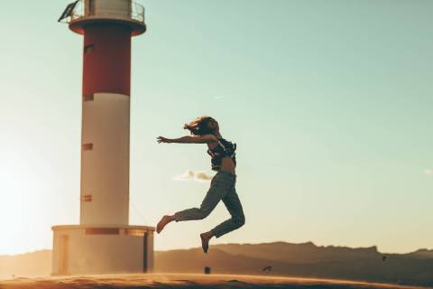 Young woman jumping in desert landscape at lighthouse model released Symbolfoto  OCAF00275
