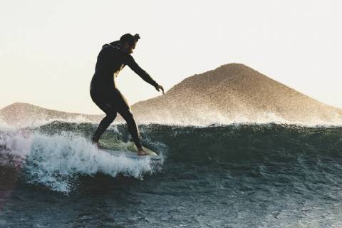 Side view shot of longboard surfer in wetsuit riding wave in sea at sunset, Tenerife Canary Islands Spain VISE003738 model released Symbolfoto Copyright: SergioxVillalba VISE003738