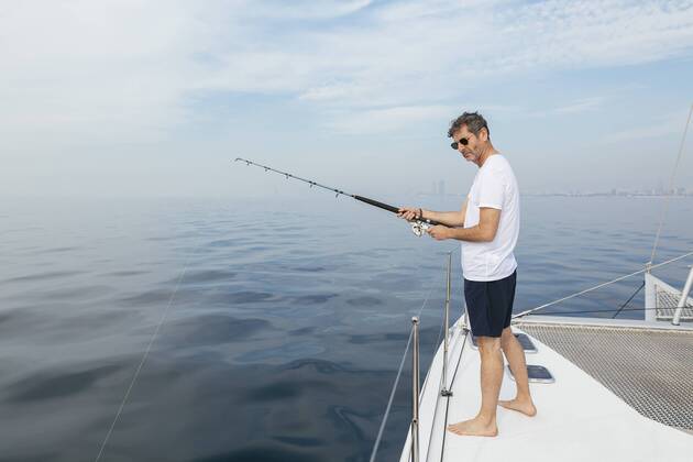 Mature man standing on catamaran, fishing model released Symbolfoto property released  EBSF02576