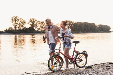 IMAGO Creative: Sommer, Abendspaziergang Young couple with bicycle wading in river model released Symbolfoto  UUF11559