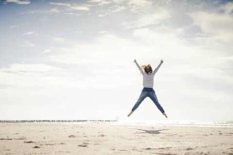 Happy woman having fun at the beach, jumping in the air model released Symbolfoto  KNSF04325
