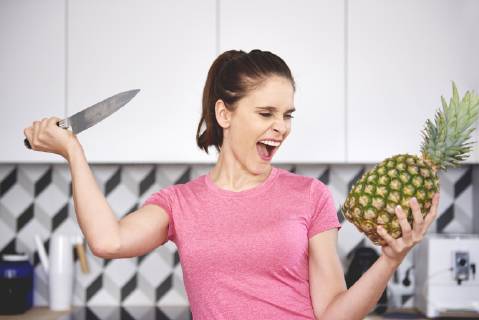 Portrait of screaming woman attacking pineapple with knife in the kitchen model released Symbolfoto property released  ABIF00787