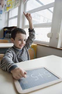 Boy sitting at desk with chalkboard, hand raised  Copyright: JérômexGorin B63825925