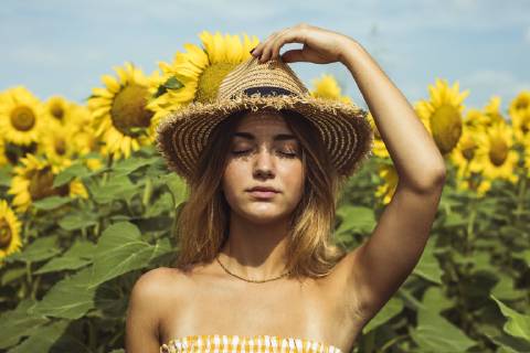Young woman holding a straw hat on her head in a field of sunflowers model released Symbolfoto  ACPF00325