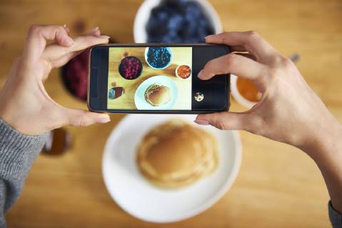 Young woman taking pictures of breakfast pancakes with berries and fresh fruit model released Symbolfoto property released  ABIF00927