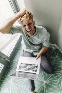 Young man sitting on ground, holding laptop, screaming in despair model released Symbolfoto property released  GUSF01293