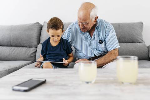 Grandfather and grandson sitting together on the couch at home looking at digital tablet model released Symbolfoto property released  JRFF01798