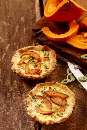  Appetizing small butternut, leek and custard quiches with a crispy pastry crust on a rustic wooden kitchen table with fresh ingredients, high angle view  Copyright: xfoodandmorex Panthermedia18037514