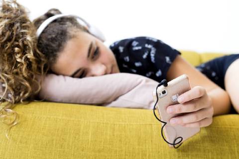 Girl lying on the couch at home listening music with headphones and smartphone model released Symbolfoto property released  ERRF00053