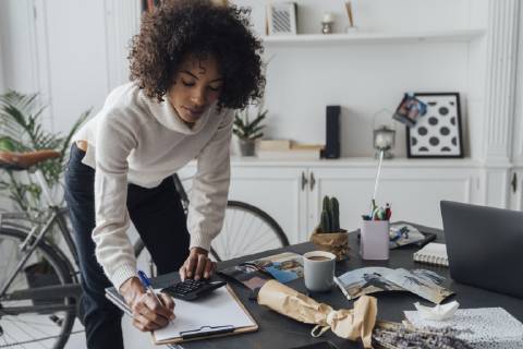 Freelancer standing at hert desk, using calculater, taking notes model released Symbolfoto property released  BOYF00930