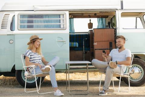 Happy young couple sitting on camping chairs at camper van with cell phone model released Symbolfoto  GUSF01577