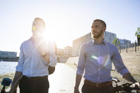 Two businessmen walking with bicycle and skateboard at the riverbank model released Symbolfoto  FKF02591