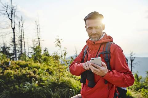 Smiling man checking his cell phone during hiking trip model released Symbolfoto  BSZF00740