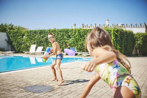 Girl and boy having a water fight with water gun and water bombs at the poolside model released Symbolfoto  DIKF00307