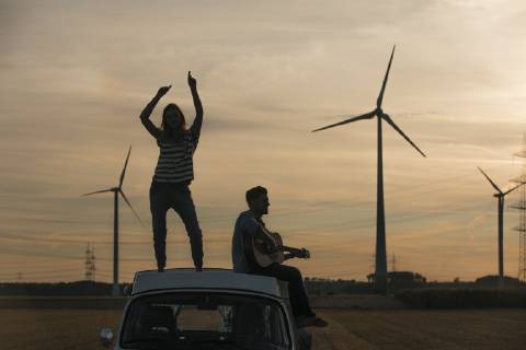IMAGO Creative: Ende des Sommers Happy couple with guitar on roof of a camper van in rural landscape at dusk model released Symbolfoto  GUSF01553