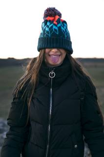 Teenage girl wearing multicolored bobble and black down jacket sticking out tongue model released Symbolfoto  ACPF00377