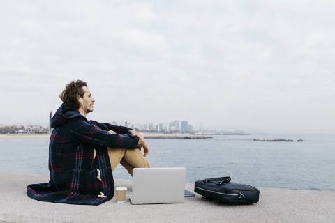 Spain, Barcelona, man with laptop, briefcase and earphones sitting at the sea model released Symbolfoto  JRFF02516
