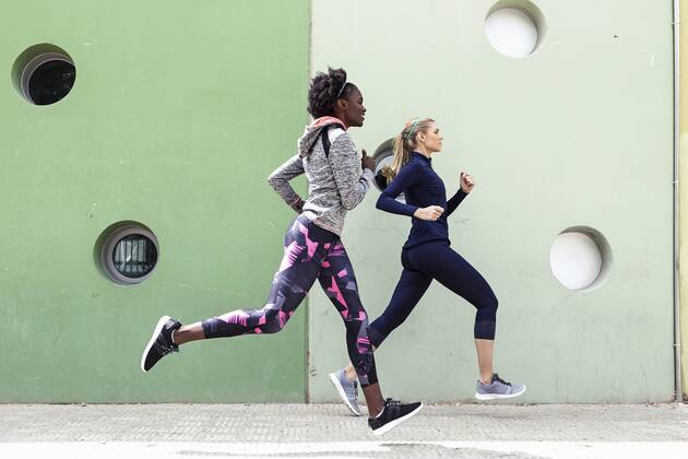 Two sporty young women running together in the city passing wall with round windows model released Symbolfoto  JSRF00139