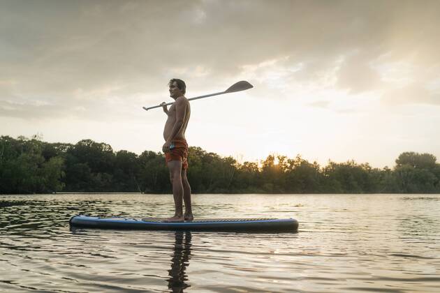 Man standing on SUP board on a lake at sunset model released Symbolfoto  GUSF01826