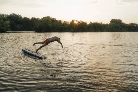 Man jumping from SUP board on a lake at sunset model released Symbolfoto  GUSF01827