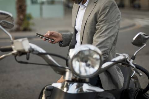 Close-up of businessman on motorscooter checking cell phone model released Symbolfoto  MAUF02041