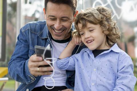 Happy father and son sharing cell phone and earbuds model released Symbolfoto  MAUF02274