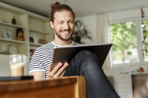 Young man with a bun sitting at home, using digital tablet model released Symbolfoto property released  PESF01140