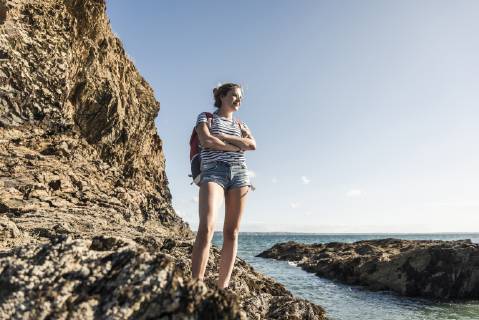 Young woman hiking on a rocky beach, looking at view model released Symbolfoto  UUF16467