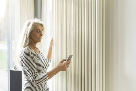 Mature woman with smartphone checking heating in living room of smart home model released Symbolfoto property released  SBOF01886