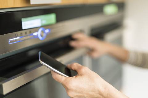 Hand of woman with smartphone checking oven in kitchen at her smart home model released Symbolfoto property released  SBOF01888