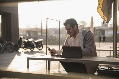 Young man using cell phone and tablet at outdoor cafe model released Symbolfoto  UUF16780
