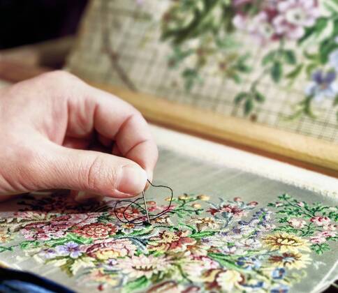 Embroidery as an old craft, close-up of a hand with an embroidery needle on an embroidery with a floral pattern.