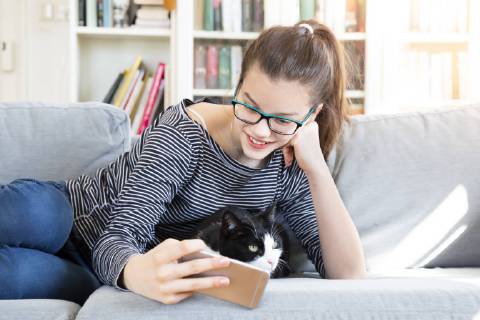 Smiling girl lying on couch at home taking selfie with cat model released Symbolfoto property released  LVF08006