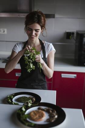 Smiling young woman garnishing plates of vegetarian food in her kitchen model released Symbolfoto property released  LJF00087