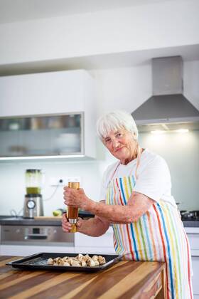  Senior woman cooking in the kitchen - eating and cooking healthy for her family putting some potates in the oven, enjoying active retirement (shallow DOF color toned image) ,model released, Symbolfoto  Copyright: xLightpoetx Panthermedia25834910