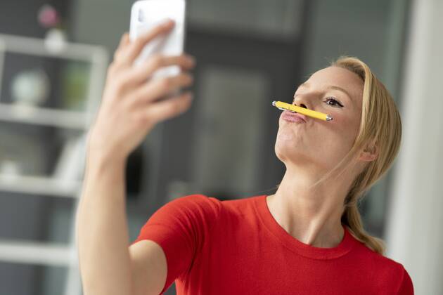 Playful young woman balancing pen on her mouth in office taking a selfie model released Symbolfoto property released  JOSF03470