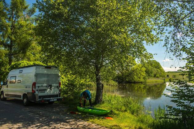 A girl pumps up her kayak next to a camping bus to paddle on the lake, Wuhrmühleweiher, Kisslegg in the Allgäu, Baden Württemberg, Germany Kayak tour at a pond in the Allgäu